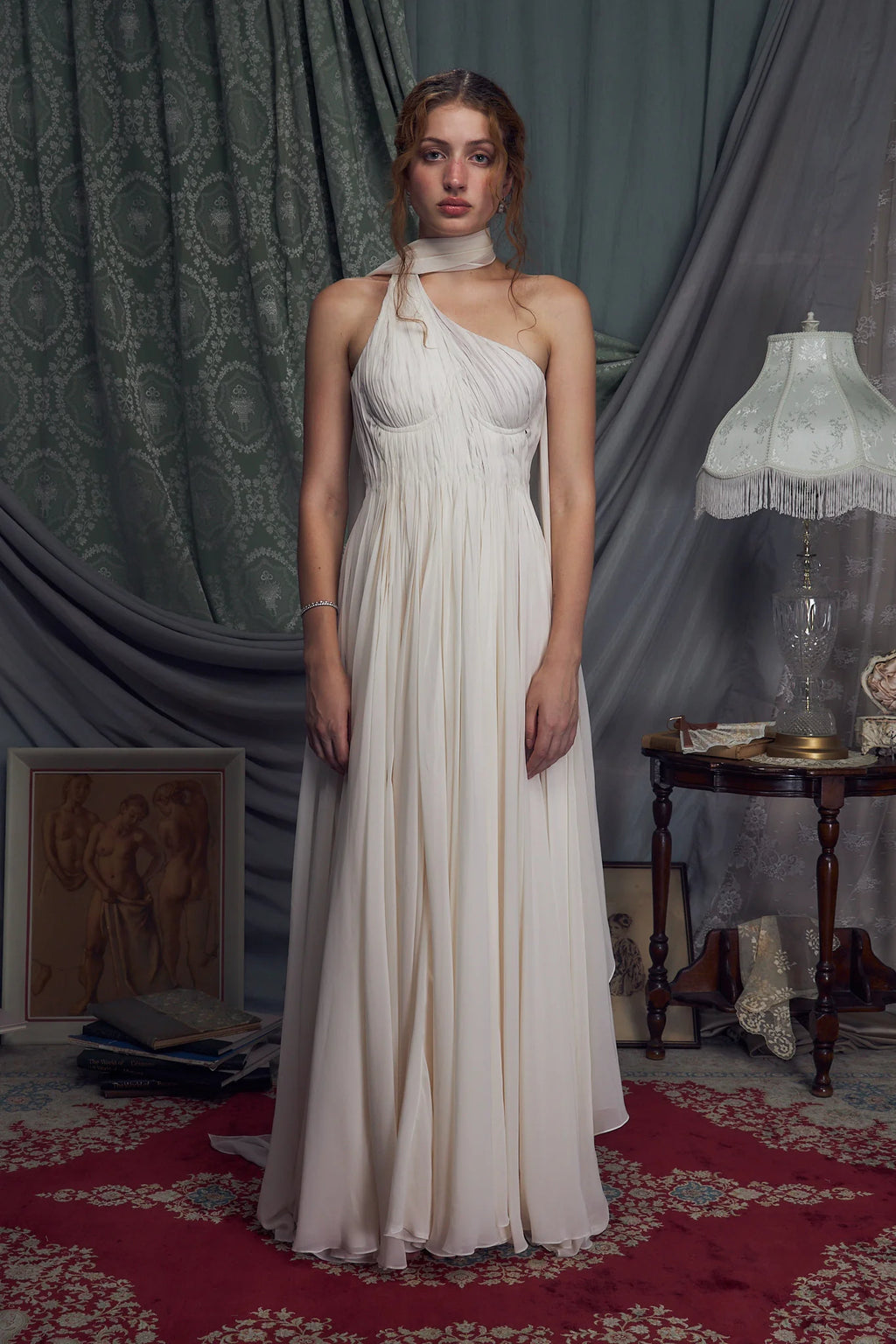 The Hellenistic Gown features a graceful one-shoulder design crafted from delicate crinkle chiffon, offering both elegance and movement. Built with underwire cups and a power mesh torso lining, it provides structured support and a flattering fit. An attached scarf adds a touch of sophistication, while the high slit accentuates leg lines for a striking silhouette. The gown secures with an invisible zipper and hook-and-eye closure at the center back, ensuring a seamless finish. 