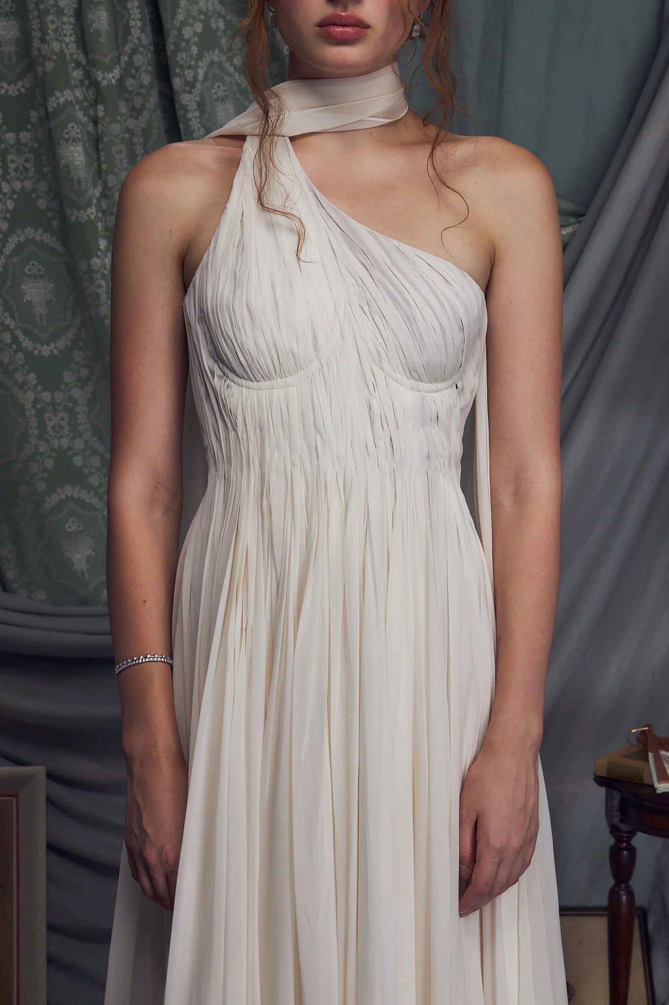 The Hellenistic Gown features a graceful one-shoulder design crafted from delicate crinkle chiffon, offering both elegance and movement. Built with underwire cups and a power mesh torso lining, it provides structured support and a flattering fit. An attached scarf adds a touch of sophistication, while the high slit accentuates leg lines for a striking silhouette. The gown secures with an invisible zipper and hook-and-eye closure at the center back, ensuring a seamless finish. 