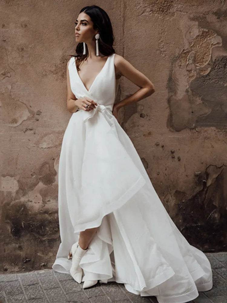 Get ready to turn heads in the Dress Safira! This simple yet stunning wedding dress features a V-neck and sleeveless design, perfect for showing off your curves. The added bow detail and backless style add an extra touch of sexiness, while the tiered skirt adds dimension and movement. Say "I do" in style.