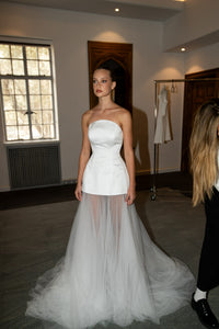 Introducing the Fabienne Gown, the perfect choice for the modern bride. This simple yet stylish gown features a corset bodice and transparent skirt, making it fashion-forward and chic. Be the center of attention on your special day with this unique wedding dress.