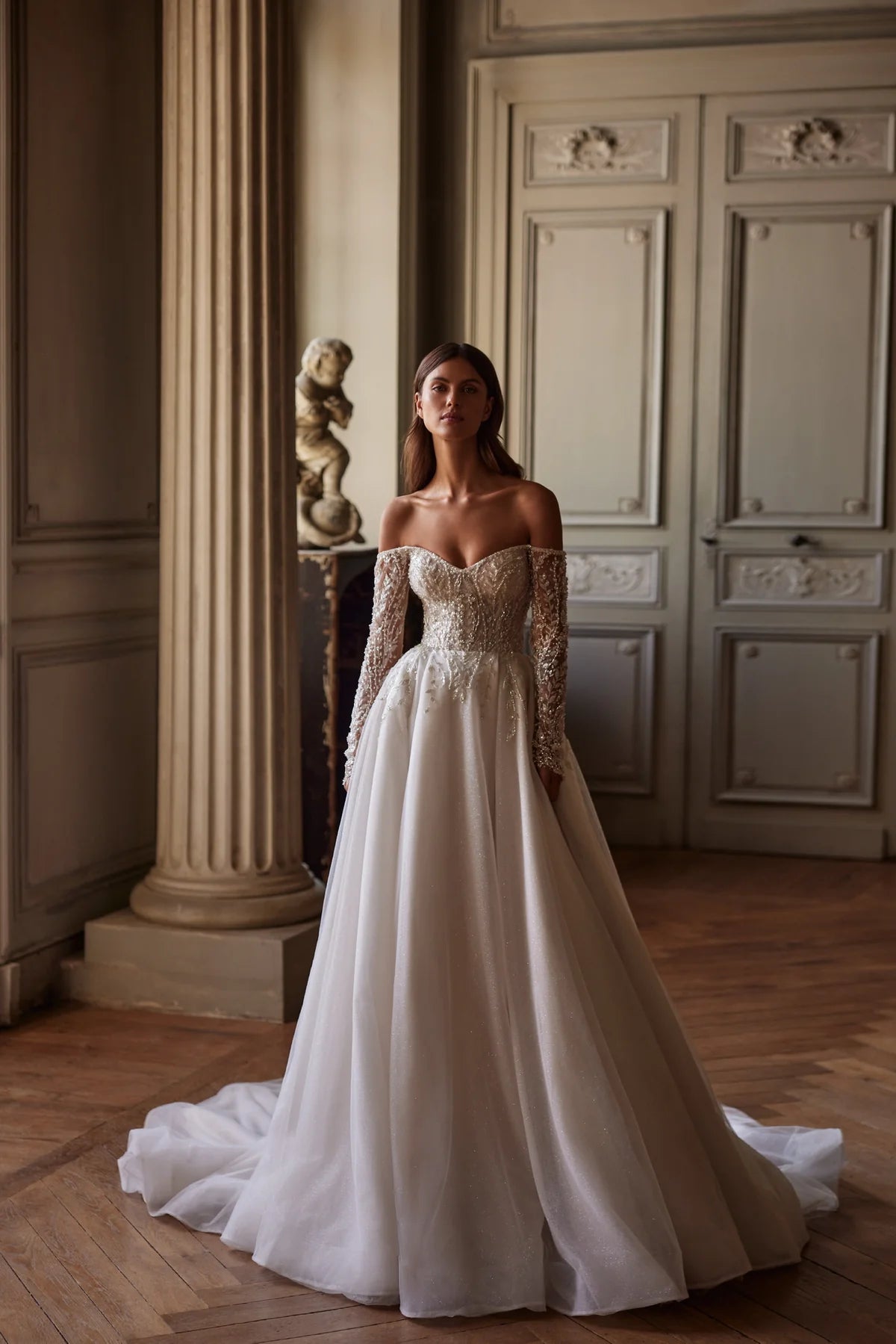 Indulge in pure elegance with the Josette Gown. A timeless A-line silhouette in ivory tone, crafted from sparkling tulle. The revealing neckline and long sleeves add a touch of sophistication. Adorned with silver lace embroidery, sequins, beads, pearls, and crystals. Tie the back zipper for a flawless fit.
