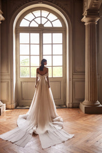 Indulge in pure elegance with the Josette Gown. A timeless A-line silhouette in ivory tone, crafted from sparkling tulle. The revealing neckline and long sleeves add a touch of sophistication. Adorned with silver lace embroidery, sequins, beads, pearls, and crystals. Tie the back zipper for a flawless fit.