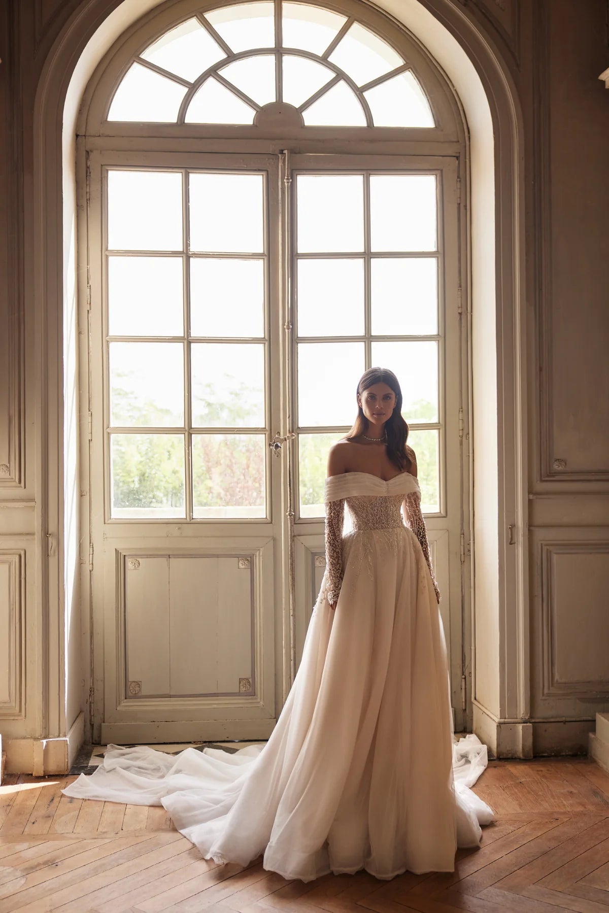 Indulge in pure elegance with the Josette Gown. A timeless A-line silhouette in ivory tone, crafted from sparkling tulle. The revealing neckline and long sleeves add a touch of sophistication. Adorned with silver lace embroidery, sequins, beads, pearls, and crystals. Tie the back zipper for a flawless fit.