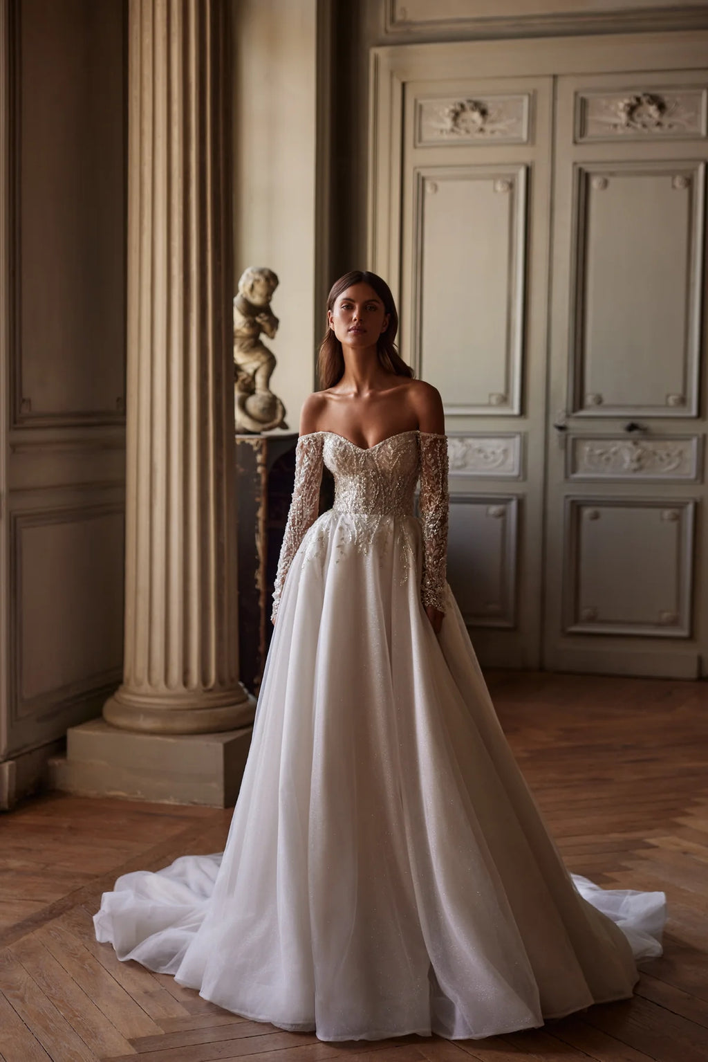 Indulge in pure elegance with the Josette Gown. A timeless A-line silhouette in ivory tone, crafted from sparkling tulle. The revealing neckline and long sleeves add a touch of sophistication. Adorned with silver lace embroidery, sequins, beads, pearls, and crystals. Tie the back zipper for a flawless fit.