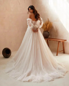 Elevate your bridal style with the Robe Vittoria. This charming A-line dress features a sweetheart neckline, intricate lace appliques, and long puff sleeves with delicate ruffles. Perfect for a boho-inspired wedding, this dress exudes elegance and romance. Say "I do" in style with the Robe Vittoria.