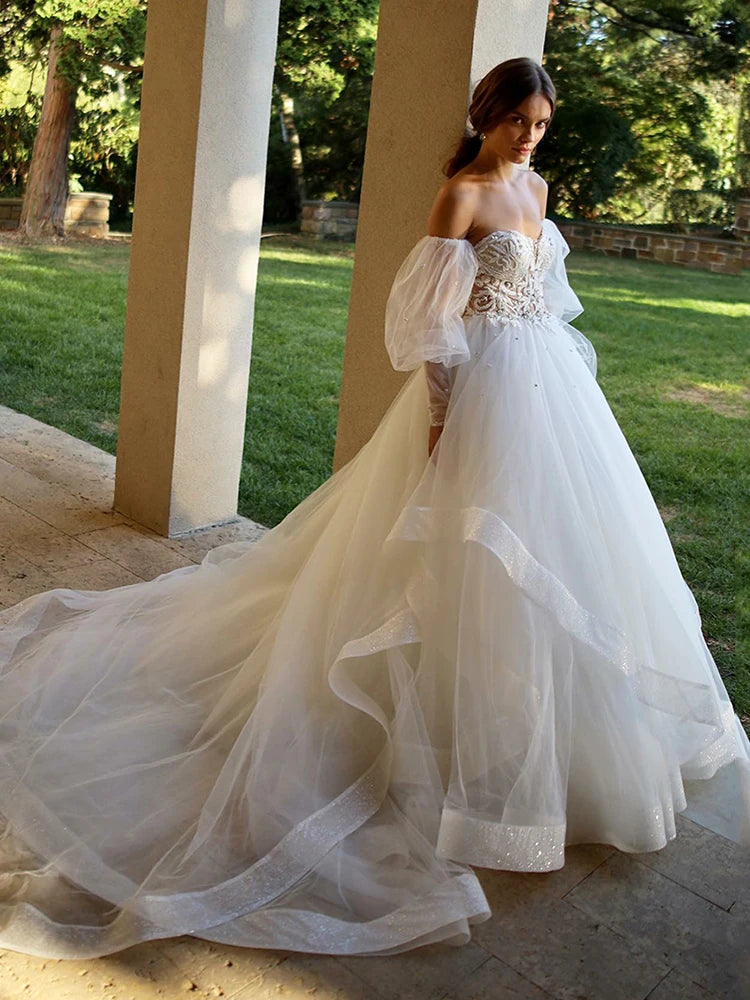 Elevate your wedding day style with the Robe Aurélie. Exquisite lace and tulle create a princess-worthy ball gown that will make you feel like royalty on your special day. The sweetheart neckline and puffed sleeves add a touch of boho charm, making this dress a dreamy choice for any bride.