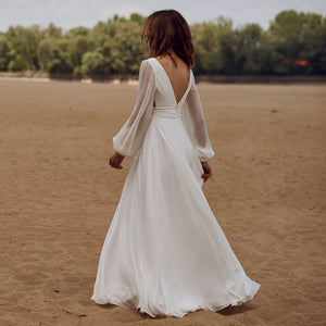 Look effortlessly elegant on your special day with our Dress Sidnea. This maxi floor length chiffon wedding dress features long bishop sleeves, a v-neckline, and a backless design for a touch of sophistication. The self-tie sash adds a feminine silhouette while the high cut showcases your figure. Say "I do" in style with this stunning dress.