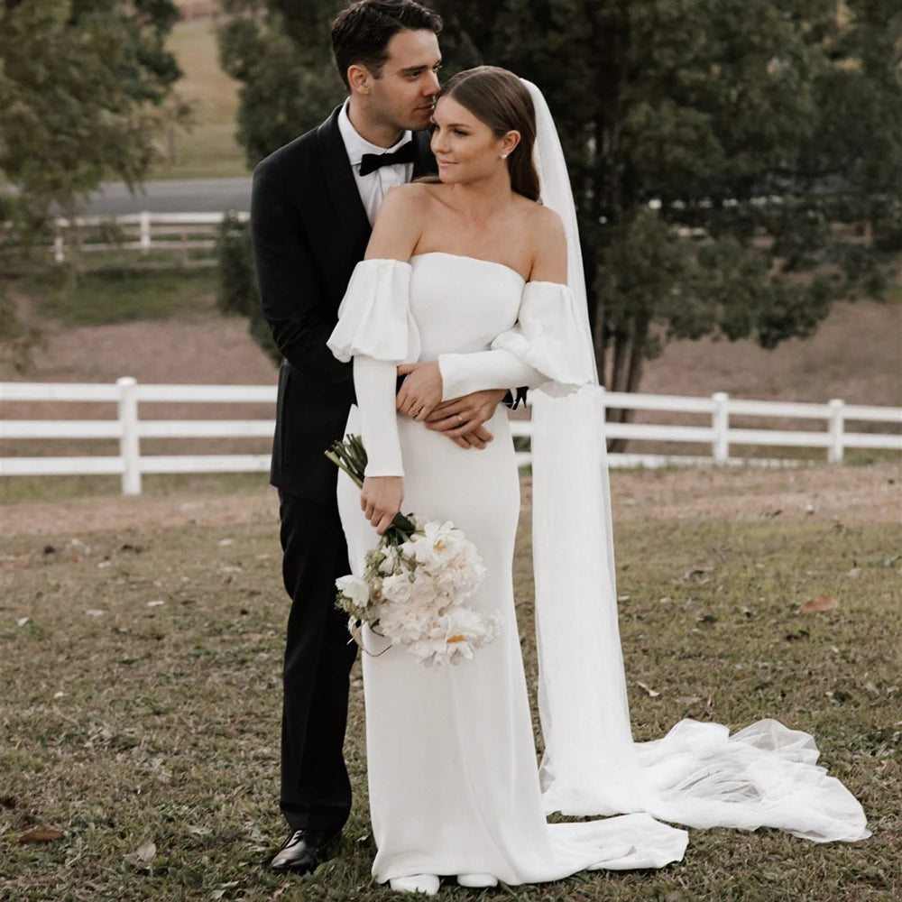 Introducing the Robe Eglantine, a minimalist wedding dress that exudes effortless elegance. This ivory crepe gown features detachable long sleeves for versatility and a sleek sheath silhouette with a brush train for a modern touch. The strapless design and buttons closure add convenience for the bride.