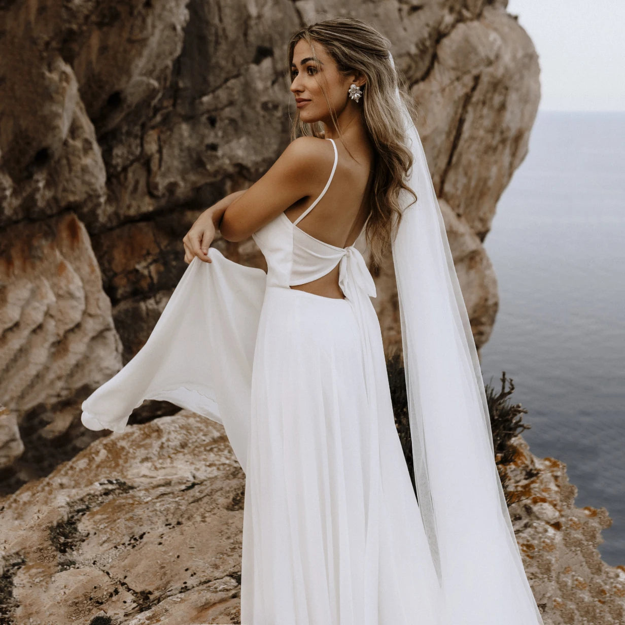 Let the perfect wedding gown inspire you with its sleek femininity! Our Robe Carolina features a spaghetti strap draped neckline, custom made brush train, ribbon tie backless, and a beach flowy silhouette. Crafted from luxurious silk chiffon, this bridal gown is perfect for a memorable day!