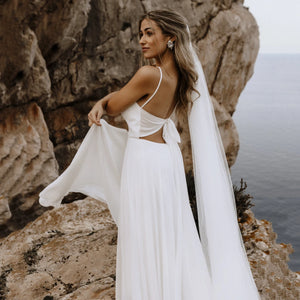 Let the perfect wedding gown inspire you with its sleek femininity! Our Robe Carolina features a spaghetti strap draped neckline, custom made brush train, ribbon tie backless, and a beach flowy silhouette. Crafted from luxurious silk chiffon, this bridal gown is perfect for a memorable day!