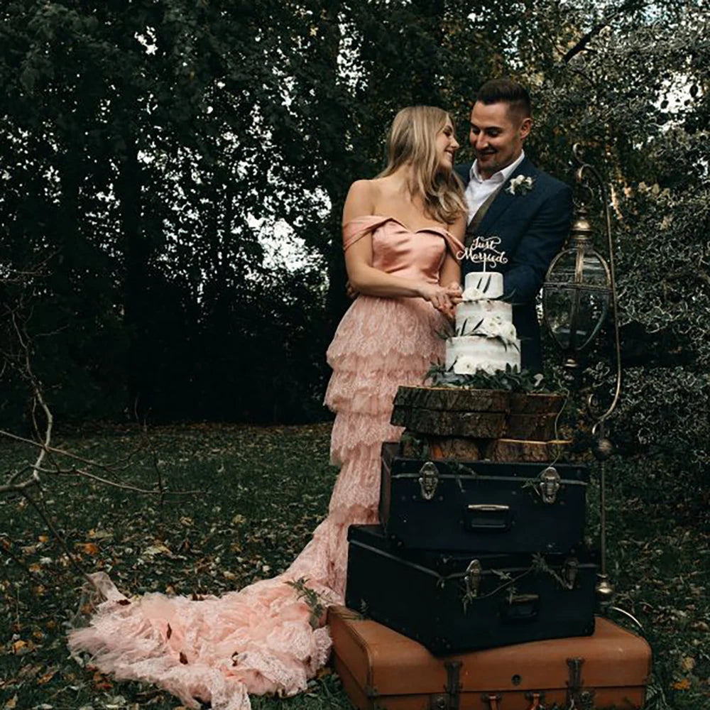 Elevate your wedding day in the exquisite off shoulder Robe Melissa. Crafted with delicate tiered lace in a dreamy mauve pink hue, this A-line custom-made gown is perfect for the plus-size bride. With a breathtaking long train and tutu details, this dress is a must-have for your elopement photoshoot.