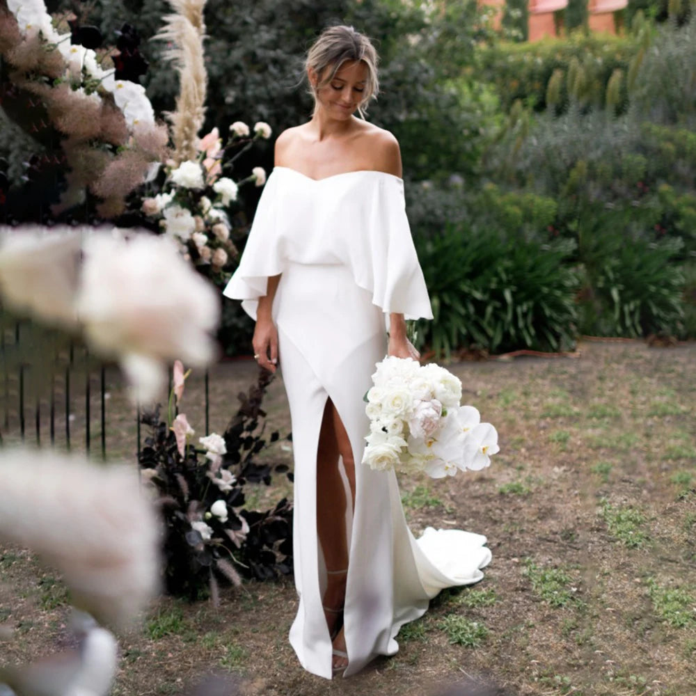 Look red-carpet ready in the captivating Sigourney robe. Featuring off-shoulder cape sleeves, a vintage crepe bodice, and a bias split open back with buttons, this gown makes an unforgettable statement. Custom made with an oversized cinched waist, take risks and be your own style icon on your big day.