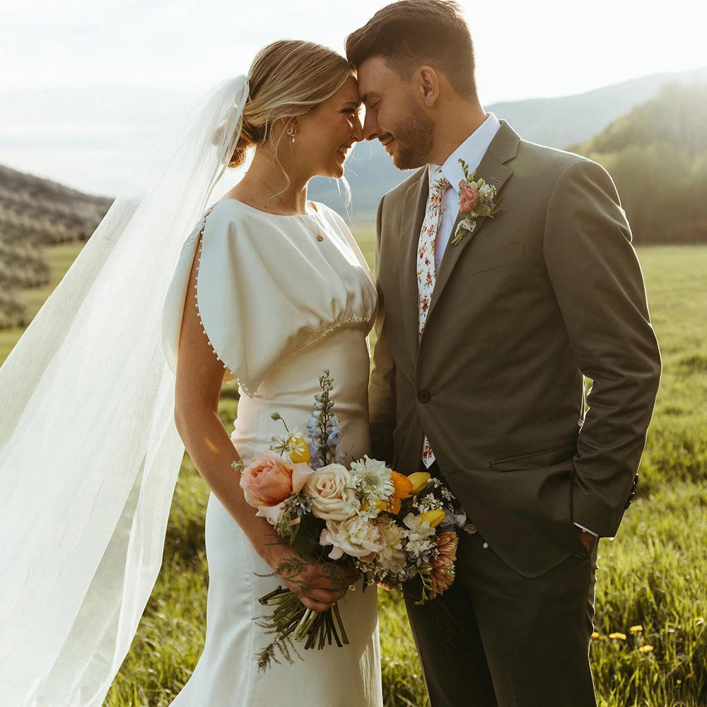 Elegant and modern, the Robe Bibi is the perfect choice for a bride looking to make a statement on her special day. With its empire waist, satin and pearl detailing, and backless design, this knee-length dress exudes both sophistication and simplicity. The slim slouch top and crepe bodycon silhouette create a figure-flattering look, perfect for a rustic or outdoor wedding.