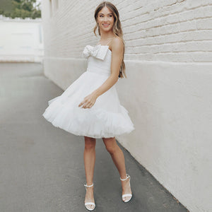 Experience the beauty and elegance of our Dress Elaina. With its beading detail, bow accents, and delicate tulle fabric, this wedding gown is perfect for a simple and charming look. The open back and spaghetti straps add a touch of playfulness, while the pearls and princess silhouette bring a sense of refinement. Say "I do" in style with this above knee bridal gown.