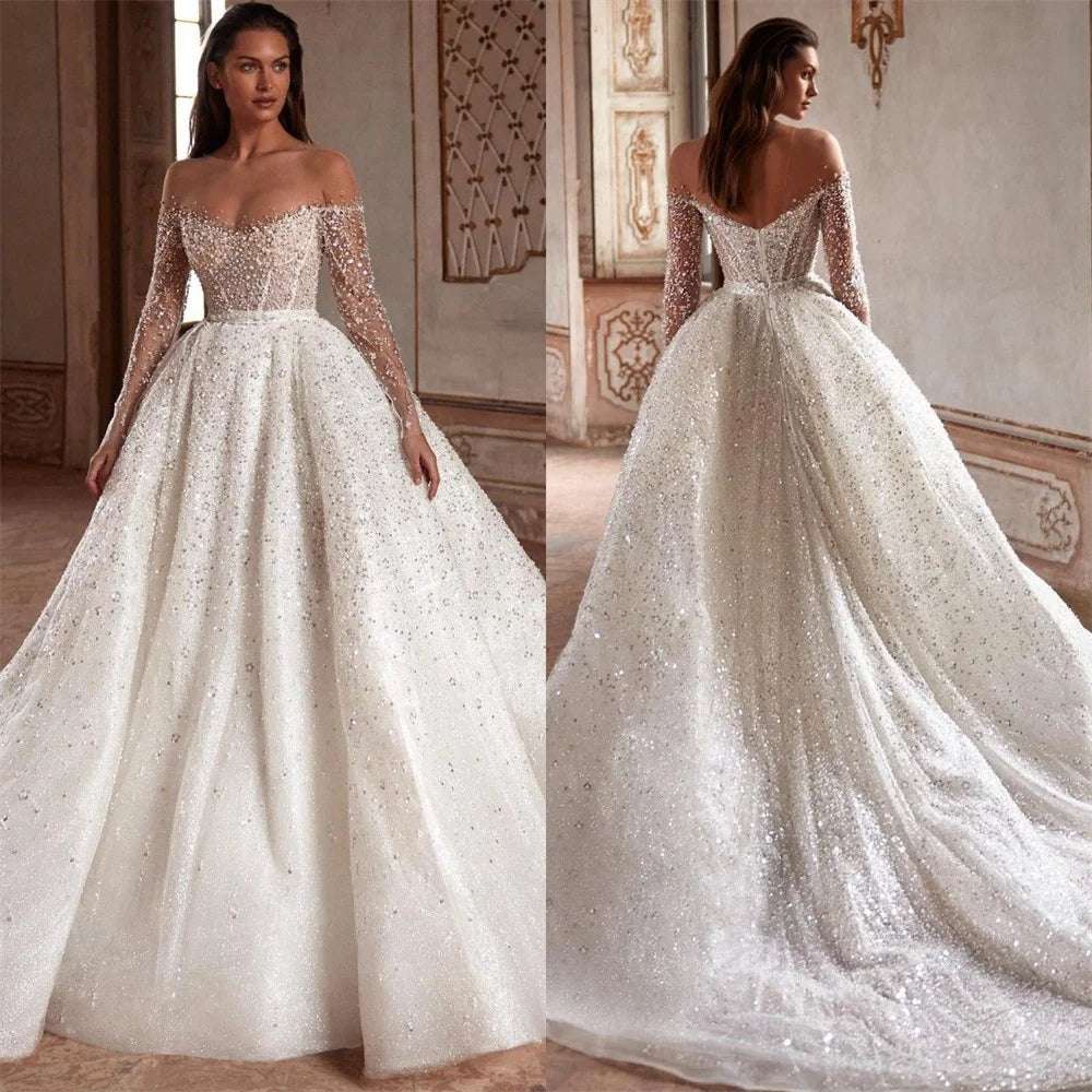 Indulge in luxury with the Robe Suzette. This elegant A-line wedding dress features an illusion neck, long sleeves, and intricate beading and pearls. Graceful and sophisticated, it's perfect for the modern bride. Complete your look with this designer gown and feel confident and stunning on your special day.