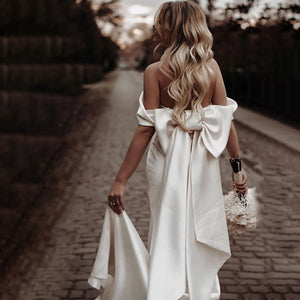 Introducing the Robe Rafaella - the perfect wedding dress for the modern bride. This elegant off shoulder sheath dress features a removable bow and is custom made to ensure the perfect fit. Made with thick satin, it offers a simple and timeless look while providing comfort and support. Say "I do" in style with the Robe Rafaella.