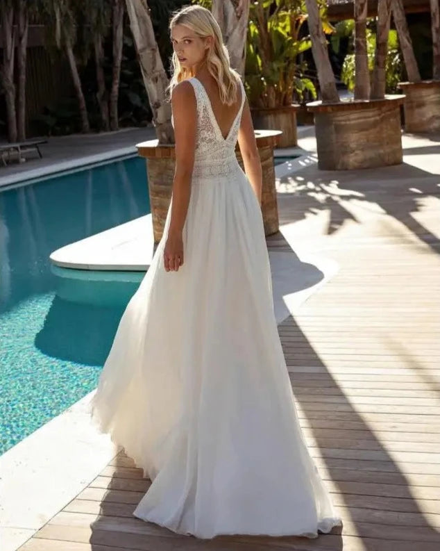 Experience true bohemian style with our Dress Elizabeth. The V-neck and backless design exudes a free-spirited vibe, while the delicate lace applique and flowy chiffon create a romantic and feminine look. Perfect for beach weddings, this sleeveless gown is sure to make you feel like a beautiful bride.