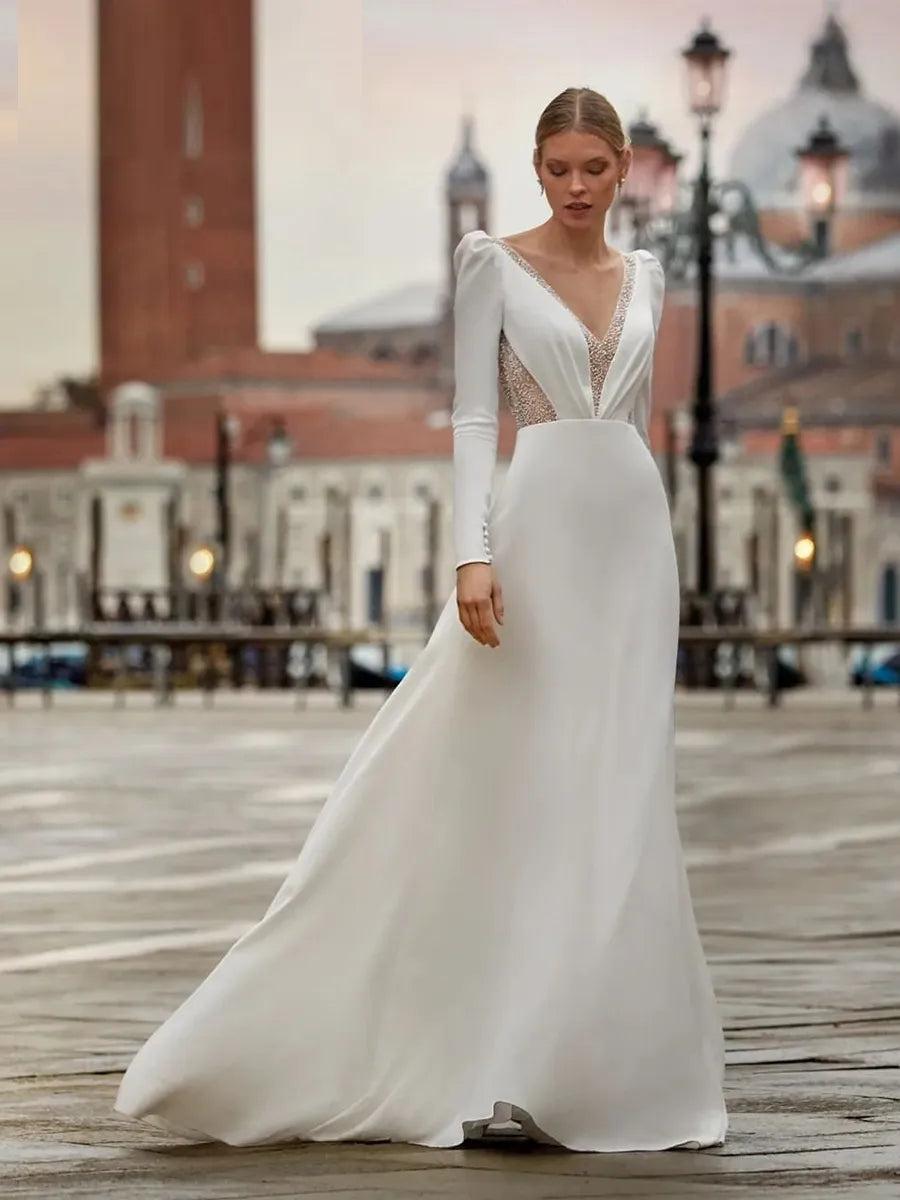 Robe Bernadette is the perfect classic wedding dress for your special day. The V-neckline, chapel-length train, full sleeves, and A-line skirt add a timeless elegance to this stunning gown. With the added touch of buttons running down the bodice, you'll be sure to make a lasting impression.