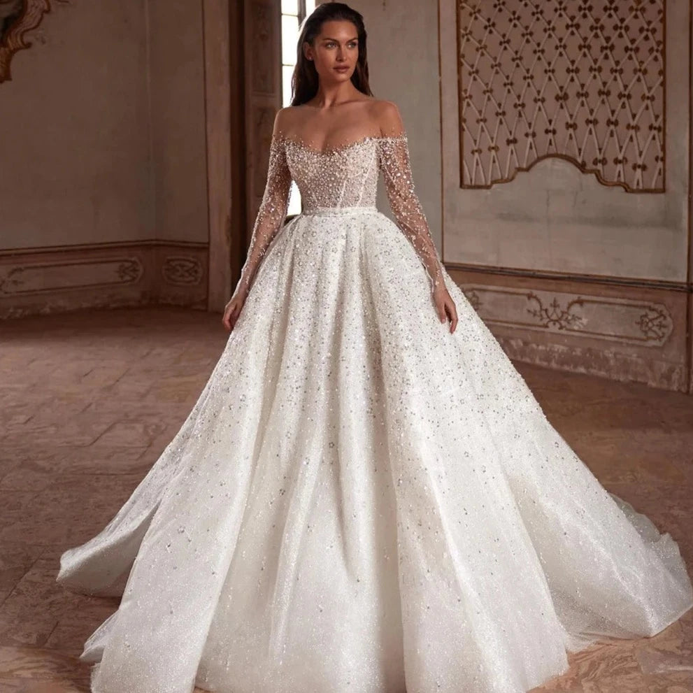 Indulge in luxury with the Robe Suzette. This elegant A-line wedding dress features an illusion neck, long sleeves, and intricate beading and pearls. Graceful and sophisticated, it's perfect for the modern bride. Complete your look with this designer gown and feel confident and stunning on your special day.
