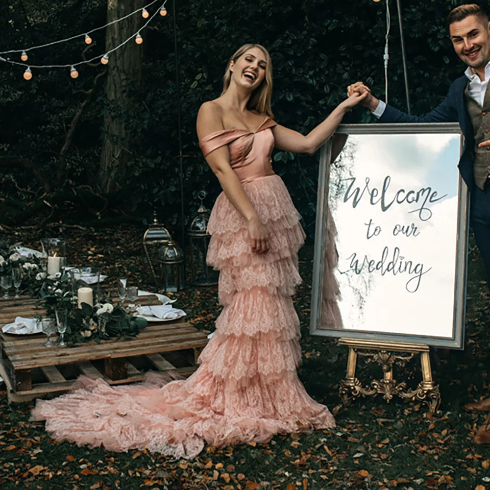 Elevate your wedding day in the exquisite off shoulder Robe Melissa. Crafted with delicate tiered lace in a dreamy mauve pink hue, this A-line custom-made gown is perfect for the plus-size bride. With a breathtaking long train and tutu details, this dress is a must-have for your elopement photoshoot.