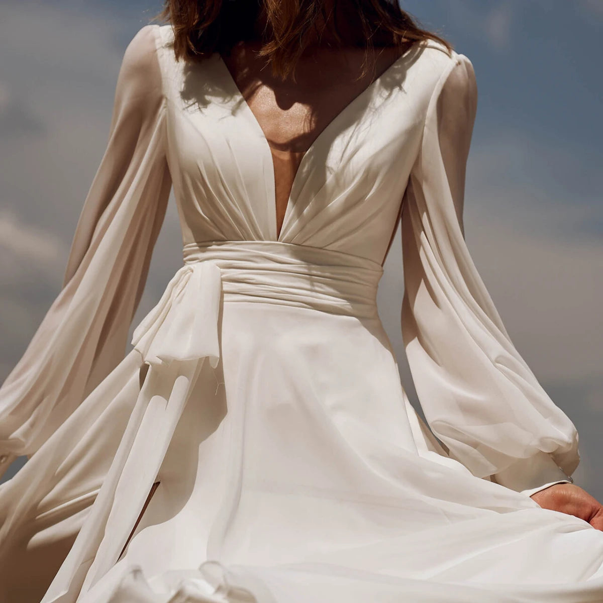 Look effortlessly elegant on your special day with our Dress Sidnea. This maxi floor length chiffon wedding dress features long bishop sleeves, a v-neckline, and a backless design for a touch of sophistication. The self-tie sash adds a feminine silhouette while the high cut showcases your figure. Say "I do" in style with this stunning dress.