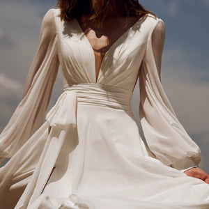 Look effortlessly elegant on your special day with our Dress Sidnea. This maxi floor length chiffon wedding dress features long bishop sleeves, a v-neckline, and a backless design for a touch of sophistication. The self-tie sash adds a feminine silhouette while the high cut showcases your figure. Say "I do" in style with this stunning dress.