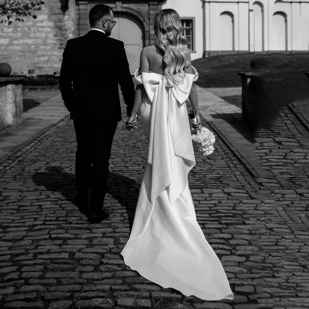 Introducing the Robe Rafaella - the perfect wedding dress for the modern bride. This elegant off shoulder sheath dress features a removable bow and is custom made to ensure the perfect fit. Made with thick satin, it offers a simple and timeless look while providing comfort and support. Say "I do" in style with the Robe Rafaella.
