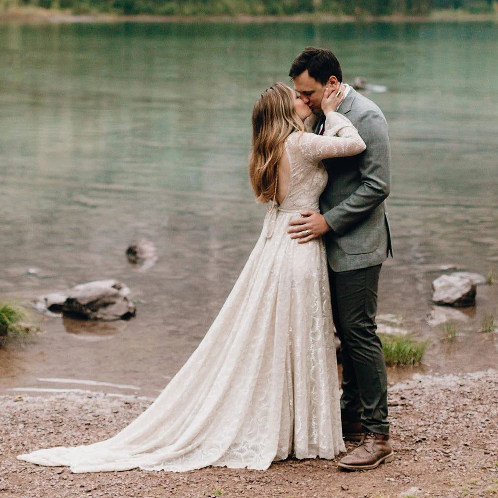 Experience the magic of your special day in our Dress Ava. The boho beach elopement design features long sleeves, a flare backless, and intricate lace with delicate pearls and tassels. The A-line silhouette and V-neckline are complemented by a custom-made belt for a perfect fit. Say "I do" in style with this unique and stunning bridal gown.