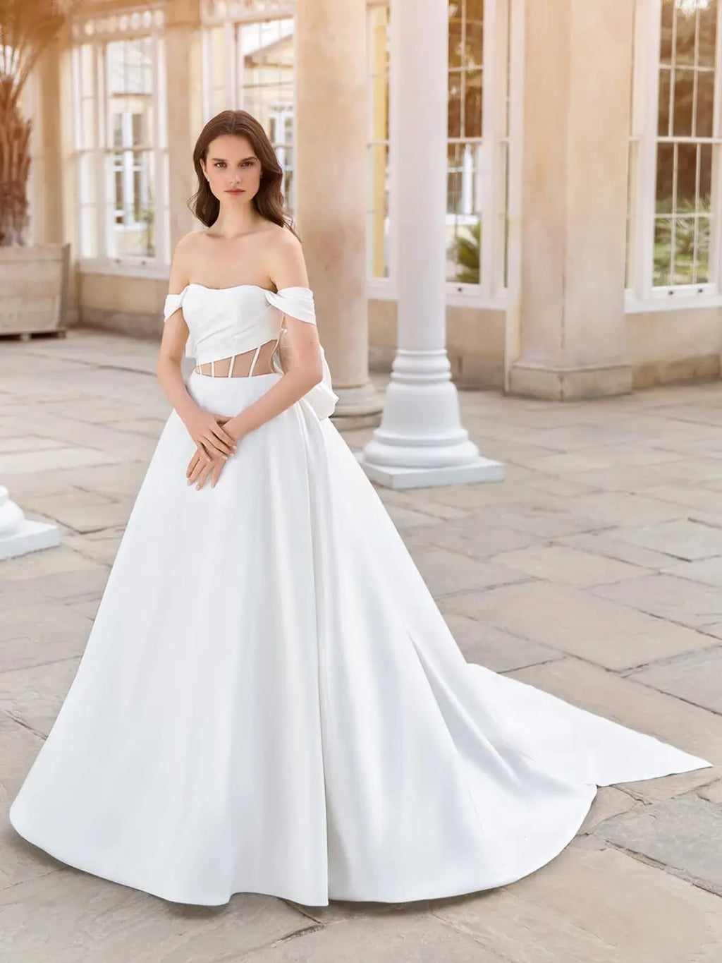 This 2-in-1 wedding dress offers versatility and style for a bride on her special day. It features a detachable ball gown with an off-shoulder design and a long, sheer tail for a dramatic entrance. The pleated bodice adds a touch of elegance and glamour, making it the perfect dress for any bride.