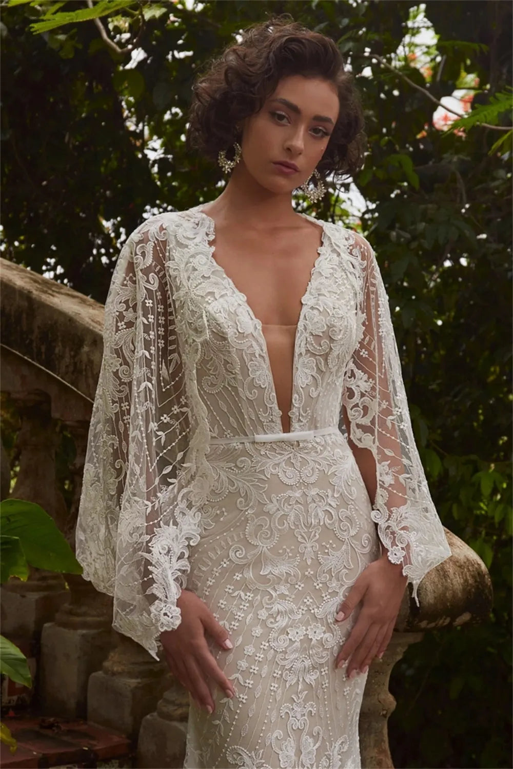 Elevate your special day in the Robe Jacqueline. This exquisite mermaid-style dress is crafted with V-neck and brush floor-length silhouette. Featuring an open back and handmade flower lace accents, this wedding dress is sure to make an unforgettable impression.