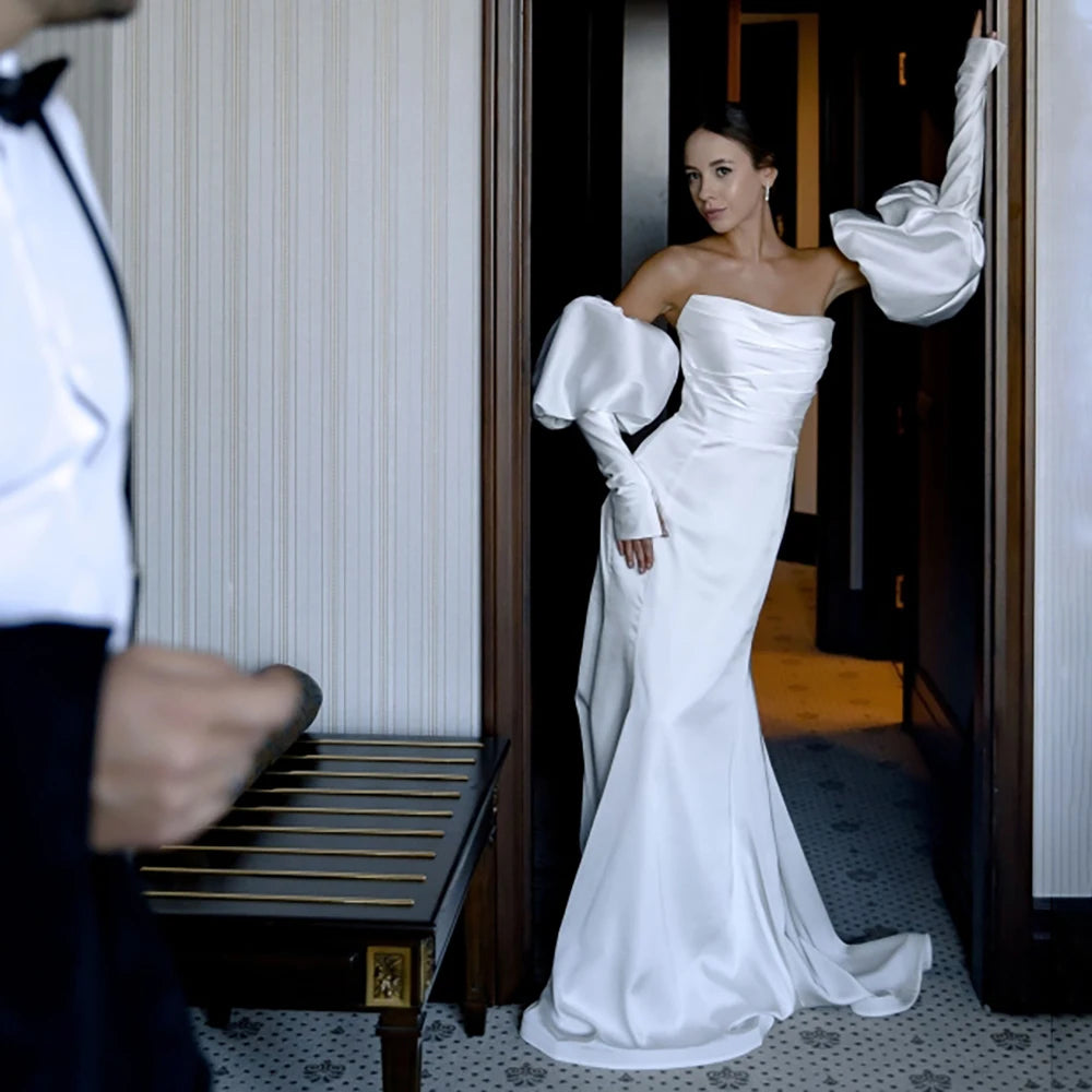 Expertly designed for the modern bride, the Robe Lucianna is a stunning strapless mermaid wedding gown made from luxurious satin. The ruched bodice sculpts and flatters the figure, while the custom made, removable lantern sleeves add an elegant touch. With a sleek zipper closure, this dress is the perfect choice for any bride looking for a timeless and sophisticated look on their special day.