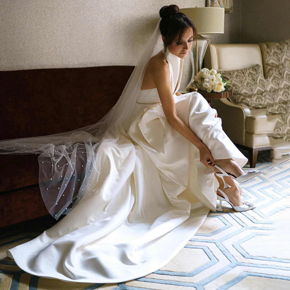 Feel like royalty in this Robe Oceane wedding dress. Handcrafted with luxurious satin, this halter high neck dress features a minimalist design for an effortlessly sophisticated look. The backless design with a large bow trailing the A-line silhouette is a timeless classic that will make you look and feel like a beautiful bride. Custom made and available in big sizes, make your special day even more special with this exquisite minimalistic yet sexy gown.