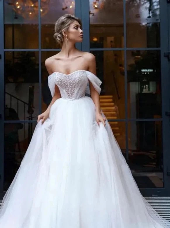 Elevate your wedding day look with our Robe Melina. This elegant ball gown boasts intricate beading, an off the shoulder sweetheart neckline, and a sleeveless tulle design. Perfect for the sophisticated bride seeking a touch of luxury and glamour.