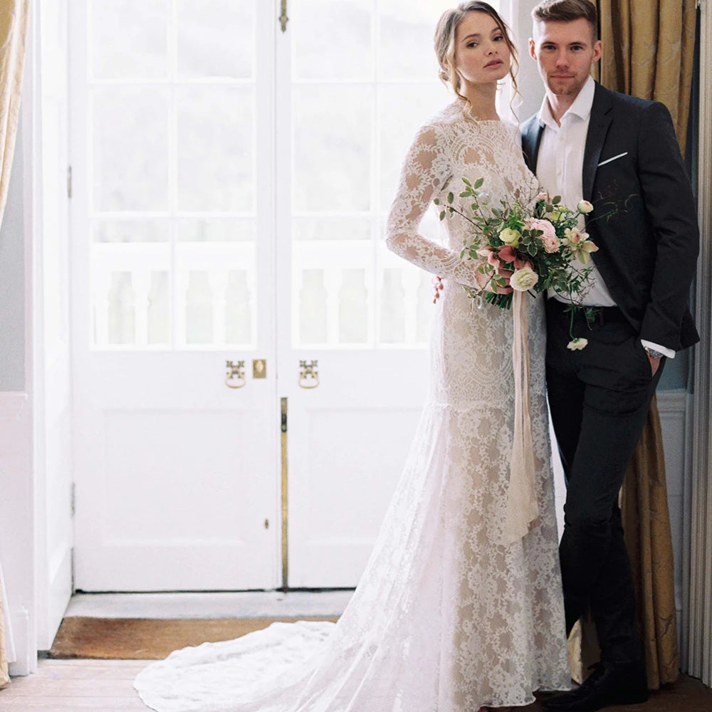 "Feel like a goddess on your special day with the Robe Ismay. This custom-made bridal gown features long lace sleeves, an open back with cutout detailing, and an illusion boat neck. The flowing chapel train and bohemian mermaid style add a touch of whimsy and romance. Say yes to the dress of your dreams!"