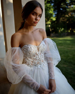 Elevate your wedding day style with the Robe Aurélie. Exquisite lace and tulle create a princess-worthy ball gown that will make you feel like royalty on your special day. The sweetheart neckline and puffed sleeves add a touch of boho charm, making this dress a dreamy choice for any bride.