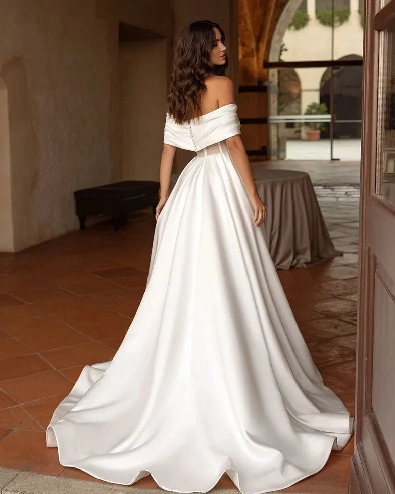 Indulge in luxury with our Robe Satine. This elegant off-the-shoulder satin gown features delicate ruching for a timeless and sophisticated look. Perfect for a stylish and stunning bridal ensemble. Experience the ultimate in bridal fashion with our Robe Satine.