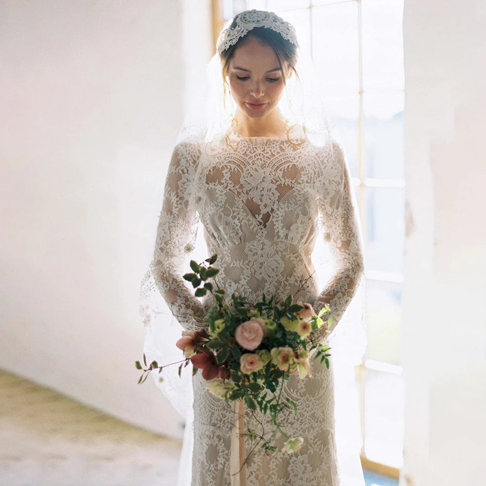 "Feel like a goddess on your special day with the Robe Ismay. This custom-made bridal gown features long lace sleeves, an open back with cutout detailing, and an illusion boat neck. The flowing chapel train and bohemian mermaid style add a touch of whimsy and romance. Say yes to the dress of your dreams!"