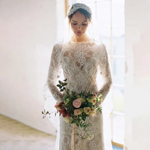 "Feel like a goddess on your special day with the Robe Ismay. This custom-made bridal gown features long lace sleeves, an open back with cutout detailing, and an illusion boat neck. The flowing chapel train and bohemian mermaid style add a touch of whimsy and romance. Say yes to the dress of your dreams!"