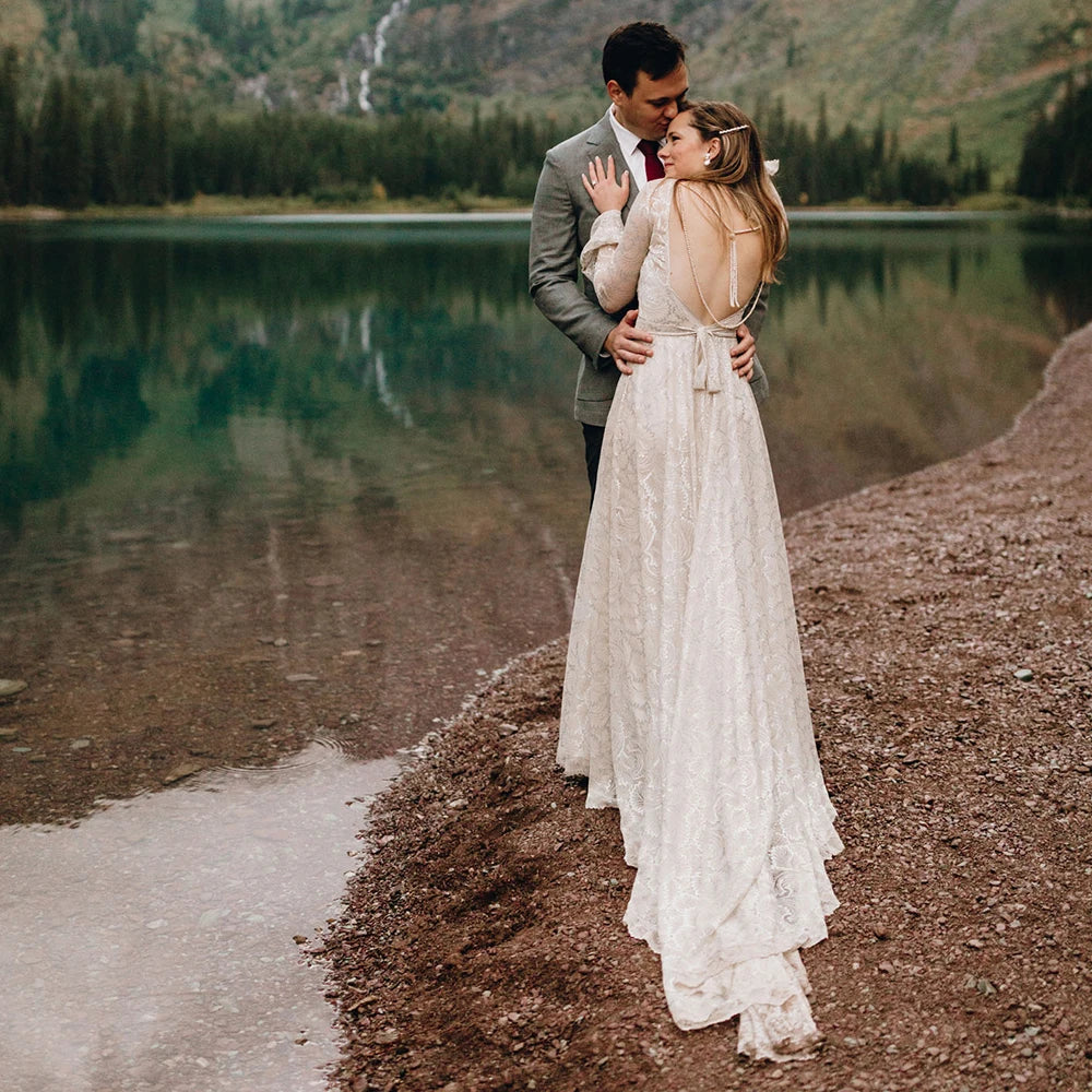 Experience the magic of your special day in our Dress Ava. The boho beach elopement design features long sleeves, a flare backless, and intricate lace with delicate pearls and tassels. The A-line silhouette and V-neckline are complemented by a custom-made belt for a perfect fit. Say "I do" in style with this unique and stunning bridal gown.