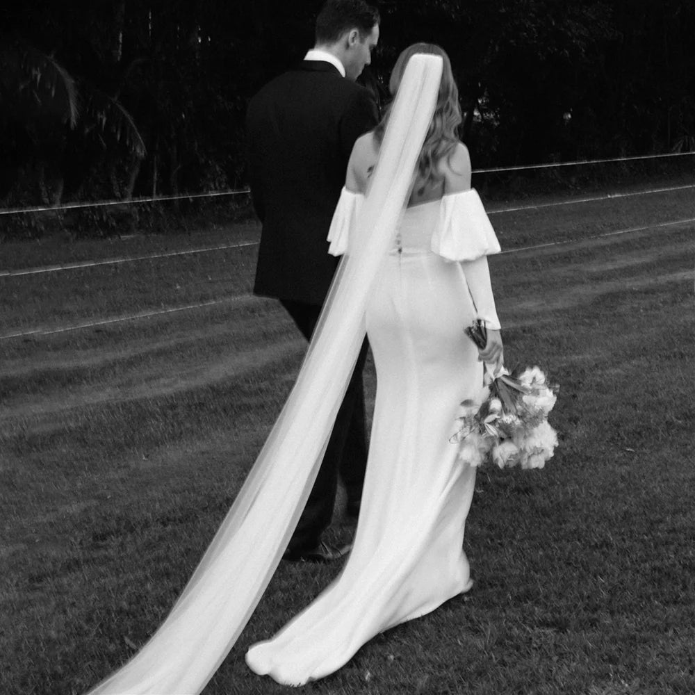 Introducing the Robe Eglantine, a minimalist wedding dress that exudes effortless elegance. This ivory crepe gown features detachable long sleeves for versatility and a sleek sheath silhouette with a brush train for a modern touch. The strapless design and buttons closure add convenience for the bride.