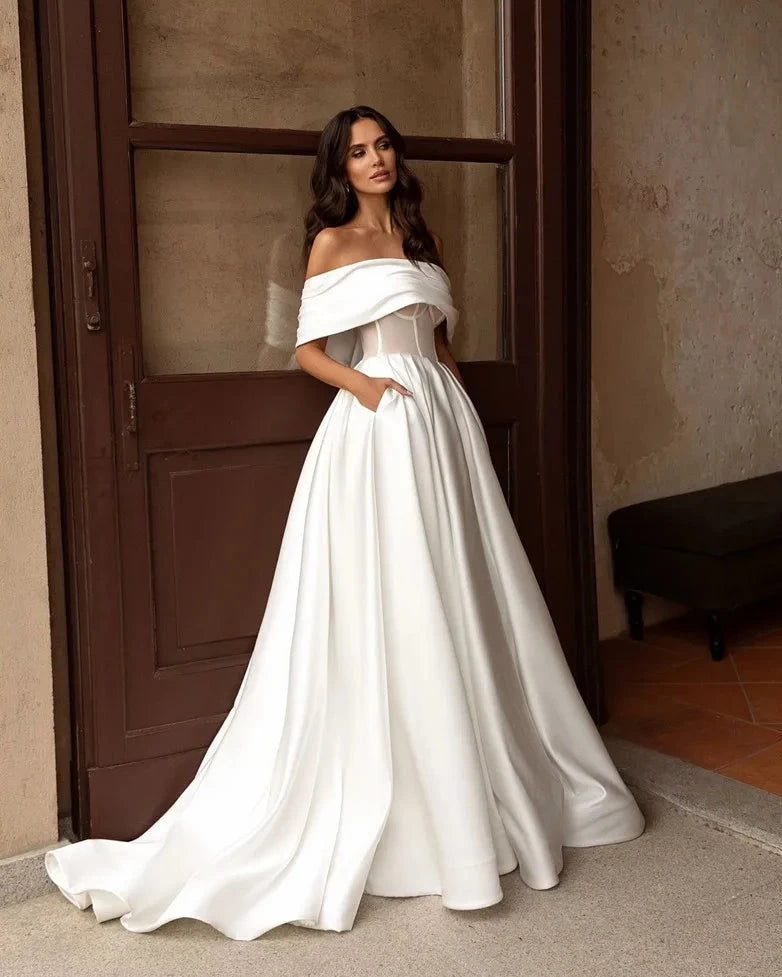 Indulge in luxury with our Robe Satine. This elegant off-the-shoulder satin gown features delicate ruching for a timeless and sophisticated look. Perfect for a stylish and stunning bridal ensemble. Experience the ultimate in bridal fashion with our Robe Satine.