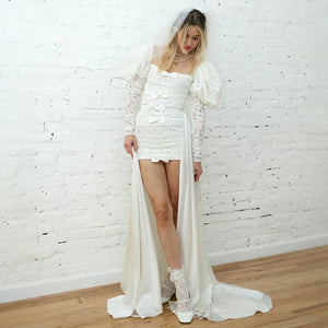 Indulge in elegance with Dress Mia: a stunning wedding dress with a sweet square neck, long fluffy sleeves, and custom-made ruching. The A-line silhouette and shirred straps create a flattering shape, while the luxurious satin fabric adds a touch of sophistication. Make your special day even more memorable with this exclusive dress.