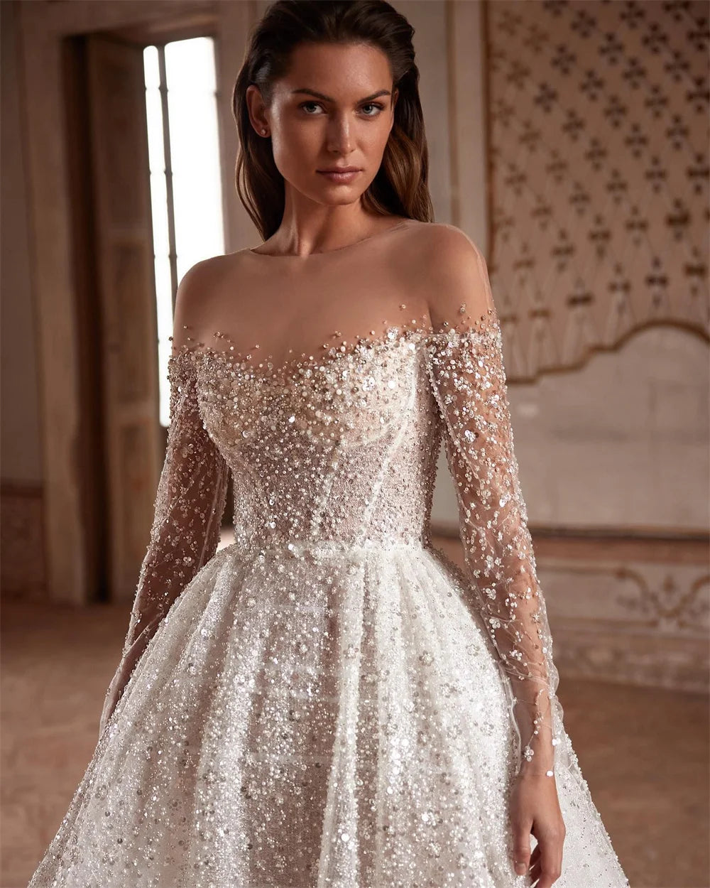 Indulge in luxury with the Robe Suzette. This elegant A-line wedding dress features an illusion neck, long sleeves, and intricate beading and pearls. Graceful and sophisticated, it's perfect for the modern bride. Complete your look with this designer gown and feel confident and stunning on your special day.
