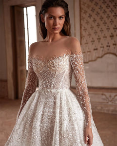Indulge in luxury with the Robe Suzette. This elegant A-line wedding dress features an illusion neck, long sleeves, and intricate beading and pearls. Graceful and sophisticated, it's perfect for the modern bride. Complete your look with this designer gown and feel confident and stunning on your special day.