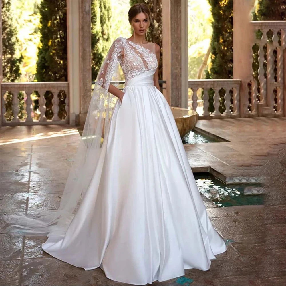 Experience luxurious elegance with our Robe Saira. This exquisite off-shoulder A-line design features playful sleeves and a sexy backless silhouette. Its fluffy texture adds a touch of sophistication to your wedding dress, making you feel confident and glamorous. Elevate your look and make a statement on your special day.