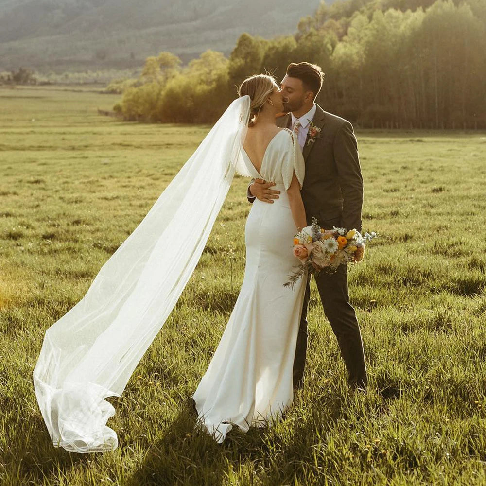 Elegant and modern, the Robe Bibi is the perfect choice for a bride looking to make a statement on her special day. With its empire waist, satin and pearl detailing, and backless design, this knee-length dress exudes both sophistication and simplicity. The slim slouch top and crepe bodycon silhouette create a figure-flattering look, perfect for a rustic or outdoor wedding.