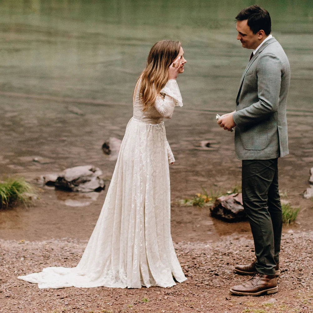 Experience the magic of your special day in our Dress Ava. The boho beach elopement design features long sleeves, a flare backless, and intricate lace with delicate pearls and tassels. The A-line silhouette and V-neckline are complemented by a custom-made belt for a perfect fit. Say "I do" in style with this unique and stunning bridal gown.