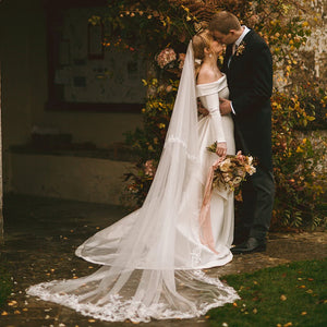 Robe Sylvaina is an exquisite wedding gown, custom-made to flatter your unique figure. Made of luxurious fabric, the dress features an off-shoulder neckline, long sleeves with delicate buttons, and a detachable overskirt train. The fitted fishtail silhouette ensures a stunning fit. Crafted with love and care to make your special day extra special.