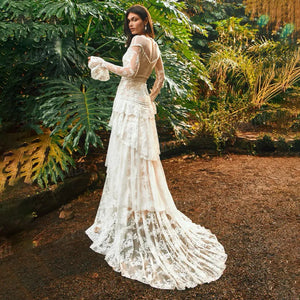 The Mila Dress is a one-of-a-kind Bohemian Lace Tulle Wedding Dress, perfect for the free-spirited bride. Made with custom tiers and long lace sleeves, this A-line dress features a backless design for a stunning and unique look. Step down the aisle in style with this beautiful and elegant bridal gown.