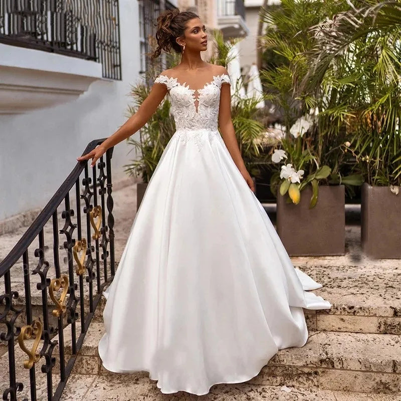 Elevate your wedding day look with the Robe Joanne. Featuring delicate lace appliques, modern satin fabric, and elegant cap sleeves, this dress offers a timeless and sophisticated style for any bride. Say "I do" in comfort and confidence with this stunning and versatile wedding dress.